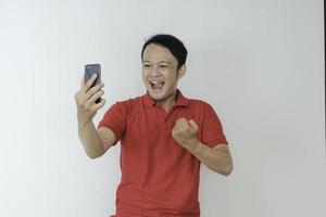 junger asiatischer mann schockiert und glücklich über das, was er auf dem smartphone auf isoliertem grauem hintergrund sieht. foto