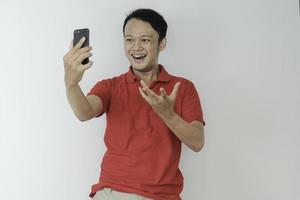 junger asiatischer mann schockiert und glücklich über das, was er auf dem smartphone auf isoliertem grauem hintergrund sieht. foto