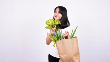 Schöne asiatische Frau mit Papiertüte mit frischem Gemüse und mit frischem Salat mit isoliertem weißem Hintergrund foto