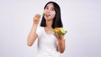 junge asiatische frau, die glücklichen essenden gesunden salat mit lokalisiertem weißem hintergrund isst foto