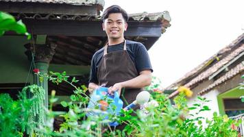 asiatischer mann, der sich darum kümmert, blumen im hausgarten zu gießen foto