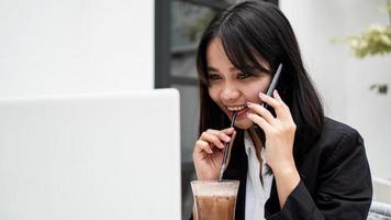 asiatische Geschäftsfrau, die Kaffee trinkt und im Café mit dem Smartphone spricht foto