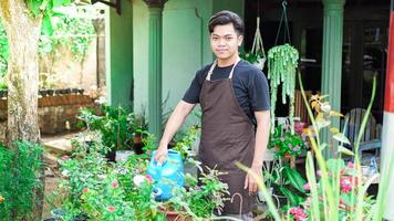 asiatischer mann, der sich darum kümmert, blumen im hausgarten zu gießen foto