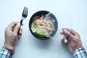 junger Mann, der Salat aus frischem Gemüse in einer Plastikschüssel isst foto