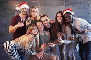 das neue Jahr kommt. Gruppe fröhlicher junger multiethnischer Menschen in Weihnachtsmützen auf der Party, die ein emotionales Lifestyle-Menschenkonzept aufwerfen foto