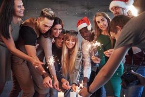 Party mit Freunden. Gruppe fröhlicher junger Leute, die Wunderkerzen und Champagnerflöten tragen foto