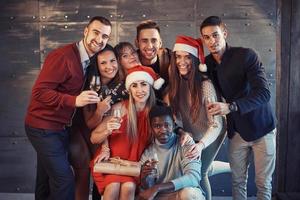 das neue Jahr kommt. Gruppe fröhlicher junger multiethnischer Menschen in Weihnachtsmützen auf der Party, die ein emotionales Lifestyle-Menschenkonzept aufwerfen foto