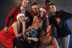 das neue Jahr kommt. Gruppe fröhlicher junger multiethnischer Menschen in Weihnachtsmützen auf der Party, die ein emotionales Lifestyle-Menschenkonzept aufwerfen