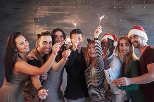Party mit Freunden. Gruppe fröhlicher junger Leute, die Wunderkerzen und Champagnerflöten tragen