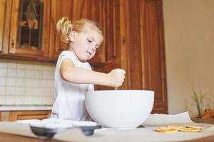 Ein kleines Mädchen bereitet einen Teig für Muffins zu. foto