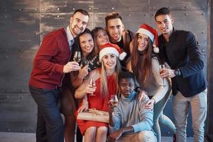 das neue Jahr kommt. Gruppe fröhlicher junger multiethnischer Menschen in Weihnachtsmützen auf der Party, die ein emotionales Lifestyle-Menschenkonzept aufwerfen foto