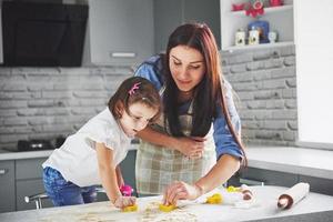 glückliche Familie in der Küche. Feiertags-Food-Konzept. mutter und tochter bereiten den teig vor, backen kekse. glückliche familie beim backen von keksen zu hause. hausgemachtes Essen und kleine Helfer foto