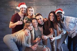 das neue Jahr kommt. Gruppe fröhlicher junger multiethnischer Menschen in Weihnachtsmützen auf der Party, die ein emotionales Lifestyle-Menschenkonzept aufwerfen
