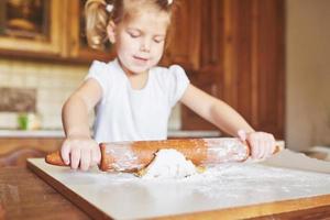 Ein glückliches Mädchen trägt einen Teig. Baby macht Abendessen im Kochanzug foto