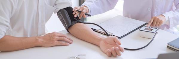 Arzt mit Blutdruckmessgerät oder Tonometer, der den Blutdruck eines Patienten misst, untersuchte den Herzschlag und sprach über die Gesundheitsversorgung im Krankenhaus.