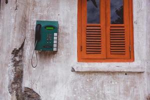 Klassisches grünes öffentliches Telefon an der alten Hauswand mit orangefarbenen Fenstern foto