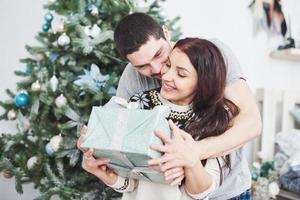 junges Paar feiert Weihnachten. Plötzlich überreichte ein Mann seiner Frau ein Geschenk. das Konzept von Familienglück und Wohlbefinden foto