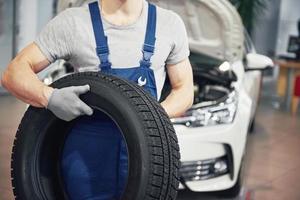 Mechaniker, der einen Reifen in der Werkstatt hält. Wechsel von Winter- und Sommerreifen foto