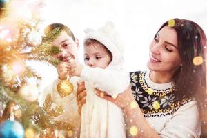 glückliche familie, die zusammen weihnachtsbaum schmückt. Vater, Mutter und Tochter. süßes Kind foto