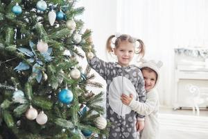 frohe weihnachten und schöne feiertage. Junge Mädchen, die beim Schmücken des Weihnachtsbaums helfen und Weihnachtskugeln in der Hand halten foto