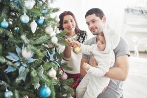 glückliche familie, die zusammen weihnachtsbaum schmückt. Vater, Mutter und Tochter. süßes Kind foto