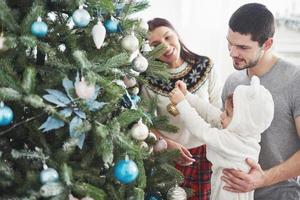 glückliche familie, die zusammen weihnachtsbaum schmückt. Vater, Mutter und Tochter. süßes Kind foto