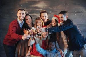 das neue Jahr kommt. Gruppe fröhlicher junger multiethnischer Menschen in Weihnachtsmützen auf der Party, die ein emotionales Lifestyle-Menschenkonzept aufwerfen foto