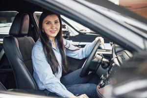 autogeschäft, autoverkauf, konsum und personenkonzept - glückliche frau, die autoschlüssel vom händler in der autoshow oder im salon nimmt foto