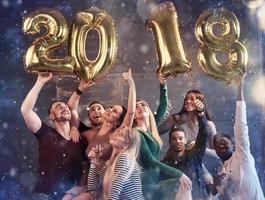 Eine Gruppe fröhlicher junger Leute hält Zahlen, die die Ankunft eines neuen Jahres 2018 anzeigen. Die Party ist der Feier des neuen Jahres gewidmet. konzepte über den lebensstil der zusammengehörigkeit der jugend foto