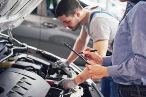 Ein Mechaniker und eine Kundin schauen sich die Motorhaube an und besprechen Reparaturen foto