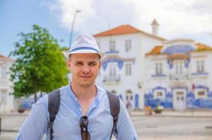 junger mann reisender mit weißem hut, der in die kamera posiert und in den straßen der stadt aveiro in portugal lächelt foto