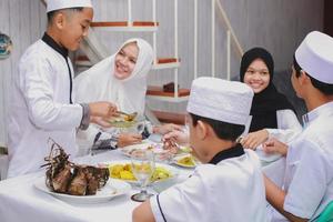 glückliche muslimische familie, die eid mubarak mit gemeinsamem essen im speisesaal feiert foto