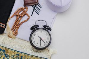 flache lage von muslim gekleidet und zubehör für salat mit gebetsperlen und uhr, die die fajr-zeit zeigt, beten foto