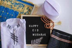 Draufsicht auf muslimische Tracht und Gebetskette auf der Gebetsmatte mit Briefbrett sagt Happy Eid Mubarak foto