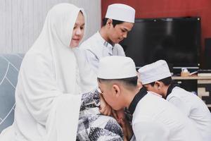 asiatische muslimische jungen, die eltern küssen, geben im haus bei eid mubarak die hand ab foto