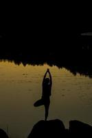 Silhouetten einer Frau, die bei Sonnenuntergang Yoga macht foto