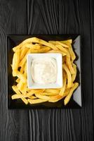 Gebratene Pommes Frites auf einem Teller mit Sauce auf schwarzem Holzhintergrund. foto