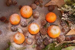 orange mandarinen auf grauem hintergrund im neujahrsdekor mit braunen tannenzapfen und grünen blättern. Weihnachtsdekoration mit Mandarinen. köstliche süße Clementine. foto