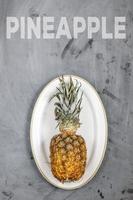 weißer teller mit reifer ganzer ananas auf grauem betonhintergrund. Wort Ananas. foto