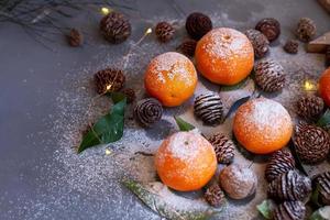 orange mandarinen auf grauem hintergrund im neujahrsdekor mit braunen tannenzapfen und grünen blättern. Weihnachtsdekoration mit Mandarinen. köstliche süße Clementine. foto