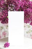 weißes Blatt in wunderschön blühendem Flieder auf einem weißen Ständer auf einem floralen Hintergrund. grußkarte, platz für text, modell