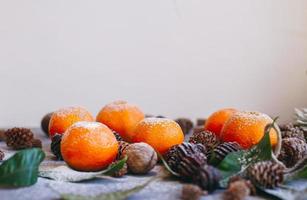 orange mandarinen auf grauem hintergrund im neujahrsdekor mit braunen tannenzapfen und grünen blättern. Weihnachtsdekoration mit Mandarinen. köstliche süße Clementine. foto
