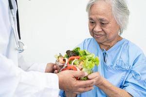 asiatische ältere oder ältere alte Dame Patientin, die gesundes Frühstücksgemüse mit Hoffnung isst und glücklich ist, während sie im Krankenhaus sitzt und hungrig auf dem Bett sitzt foto