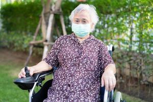 asiatische seniorin oder ältere alte dame patientin auf elektrischem rollstuhl mit fernbedienung und tragen einer gesichtsmaske zum schutz der sicherheitsinfektion covid 19 coronavirus. foto
