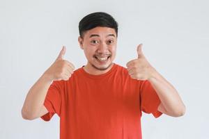 glücklicher asiatischer mann, der rotes t-shirt mit daumen hoch geste auf weißem hintergrund trägt foto