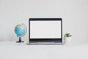 Laptop mit leerem Bildschirm zwischen Mini-Globus und Sukkulenten isoliert auf weißem Hintergrund foto