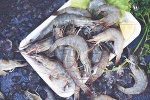 Rohe Garnelen auf Teller Plastikschale, frische Garnelen Garnelen zum Kochen mit Gewürzen Zitronengemüsesalat Salat auf dunklem Hintergrund im Fischrestaurant foto