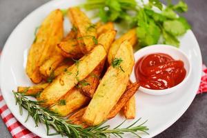 Kartoffelkeile auf weißem Teller mit Rosmarin-Kräuter-Koriander und Tomaten-Ketchup-Sauce, Kochen von Pommes Frites oder Bratkartoffeln foto