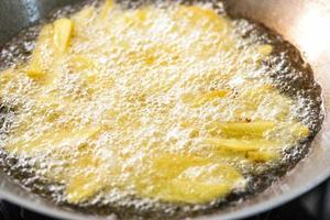 Pommes Frites kochen oder Kartoffeln in heißem Öl für Kartoffelecken braten, Nahaufnahme Bratkartoffeln in Öl auf Pfanne foto