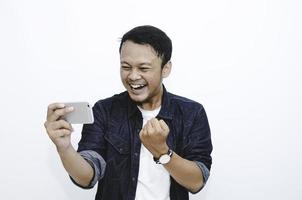 lächeln und glückliches gesicht des jungen asiatischen mannes beim spiel am telefon in der hand. foto
